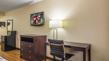 A hotel room with a desk, chair, dresser, and a flat-screen TV mounted on the wall.