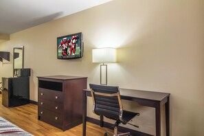 A hotel room with a desk, chair, dresser, and a flat-screen TV mounted on the wall.