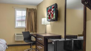 A hotel room with a bed, a desk, a chair, a television mounted on the wall, and a window with curtains. - Red Roof Inn Perrysburg (Perrysburg)