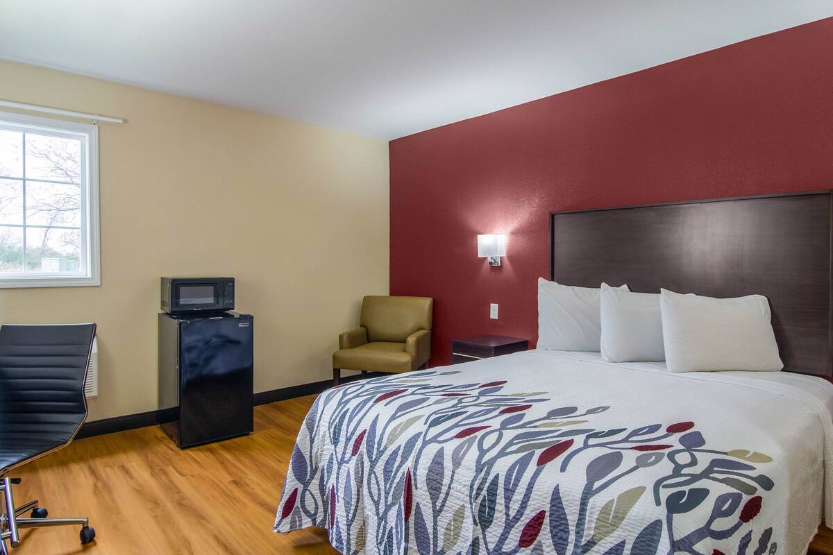 Quarto de hotel com cama, uma cadeira, escrivaninha e janela.