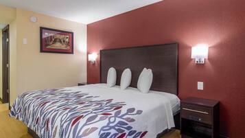 A hotel room with a bed, a nightstand, a wall-mounted lamp, and a framed picture on the wall.