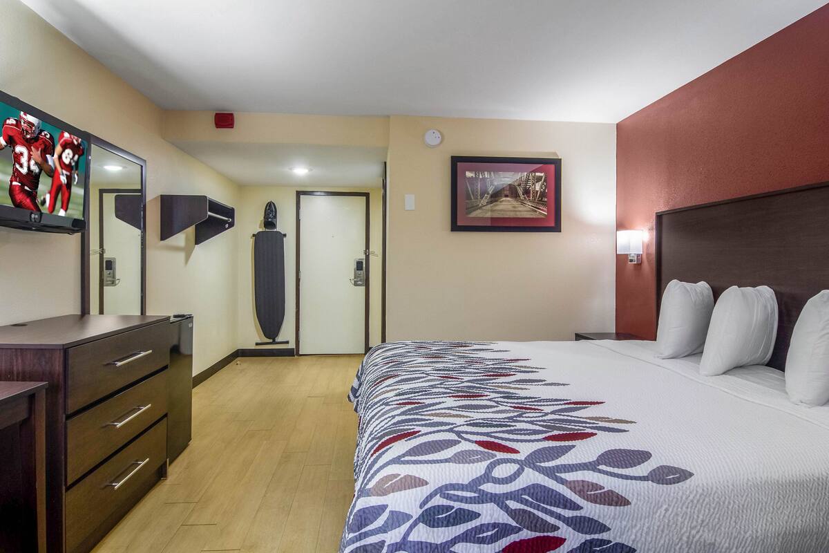 Quarto de hotel com uma cama grande, cômoda, espelho, porta e quadro pendurado na parede.