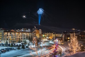 Hotelli, jossa on useita kerroksia, parkkipaikka ja näkymä lumihuippuiselle vuorelle yöllä.
