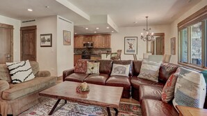 A spacious living room with a brown leather sofa set, a wooden coffee table, and a patterned rug. - Elegant Updated 3 Bedroom Condo At One Arrowhead Place Condo by RedAwning (Edwards)
