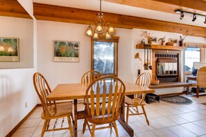 Enjoy a warm and inviting dining area with a fireplace, framed artwork, and a large window offering a view of the surrounding mountains.