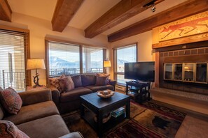 A cozy living room with a fireplace, a sofa set, a television, and large windows with blinds. - View Of Red Mountain From 2 Br  2 Bedroom Condo - No Cleaning Fee! by RedAwning (Crested Butte)