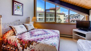 Quarto com cama grande, televisão e janela com vista para edifícios.