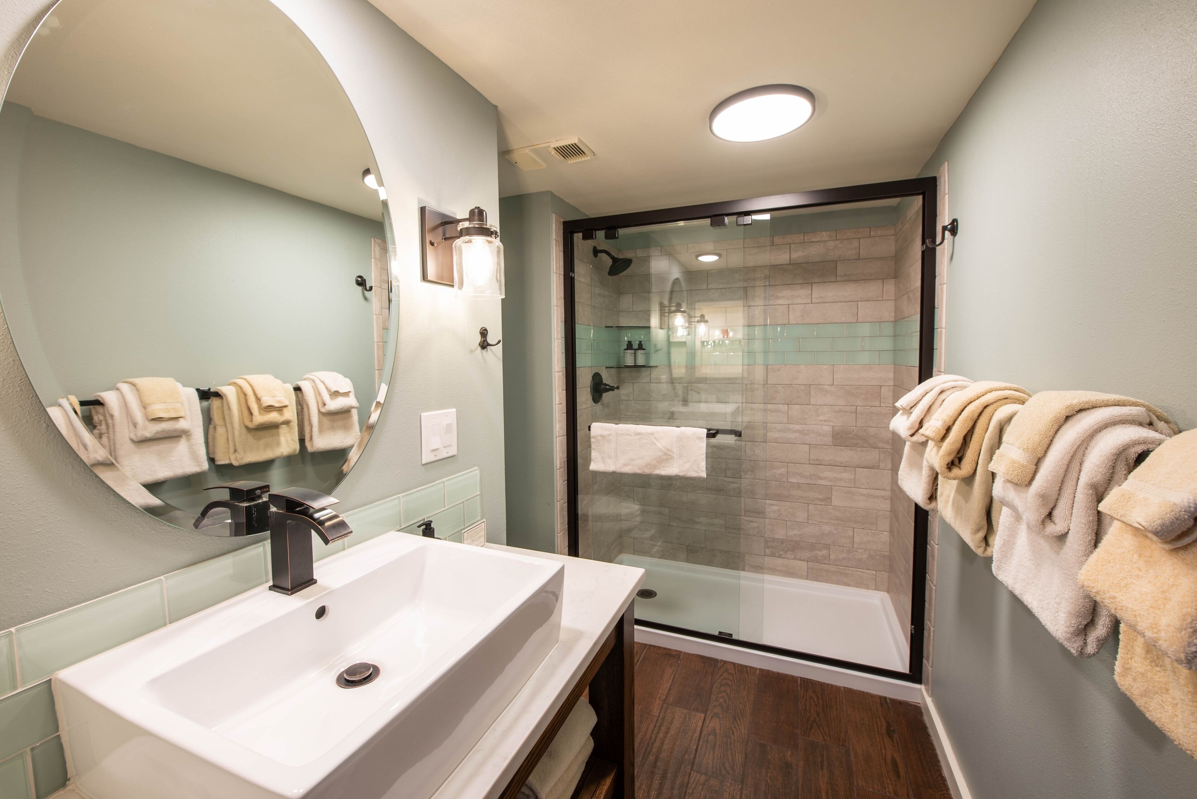 A bathroom with a large sink, a glass shower enclosure, and towels hanging on the wall.