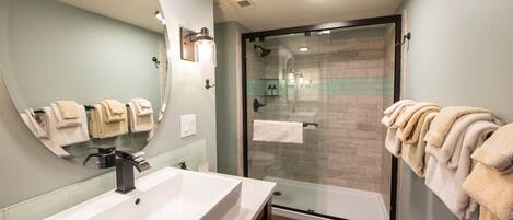 A bathroom with a large sink, a glass shower enclosure, and towels hanging on the wall.