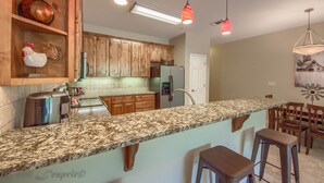 A kitchen with wooden cabinets, granite countertops, a stainless steel refrigerator, and pendant lighting. - Riverview Terrace Rg 203 3 Bedroom Condo by RedAwning (New Braunfels)