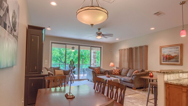 A spacious living room with a dining table, a sofa, and a ceiling fan. - Riverview Terrace Rg 203 3 Bedroom Condo by RedAwning (New Braunfels)