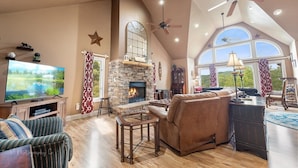 A spacious living room with a stone fireplace, a large flat-screen TV, and a high ceiling with skylights. - Enchanted Primrose 2 Bedroom Chalet by RedAwning (Sevierville)
