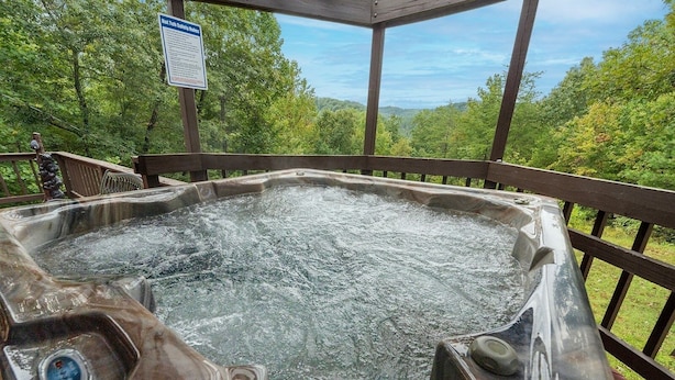 A hot tub on an outdoor deck with a wooden railing, surrounded by lush greenery. - Enchanted Primrose 2 Bedroom Chalet by RedAwning (Sevierville)