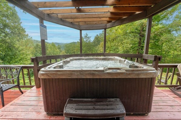 A hot tub on a wooden deck with a view of a forested landscape.