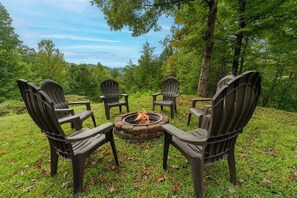 A circular fire pit surrounded by four Adirondack chairs in a grassy outdoor area with trees in the background. - Enchanted Primrose 2 Bedroom Chalet by RedAwning (Sevierville)