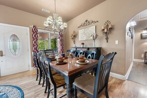 A dining room with a wooden table set for six, surrounded by chairs, a chandelier, and wall-mounted sconces. - Enchanted Primrose 2 Bedroom Chalet by RedAwning (Sevierville)
