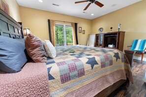 Un dormitorio con una cama grande, un ventilador de techo, un televisor y vistas al exterior a través de una ventana.