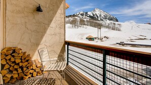 A balcony with a view of a snow-covered mountain, a chair, and a stack of firewood. - 1 Br + Loft With Mountain Views 1 Bedroom Condo - No Cleaning Fee! by RedAwning (Crested Butte)