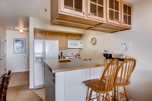 A kitchen with wooden cabinets, a refrigerator, a microwave, and a stove. There are two wooden chairs at the kitchen island. - 1 Br + Loft With Mountain Views 1 Bedroom Condo - No Cleaning Fee! by RedAwning (Crested Butte)