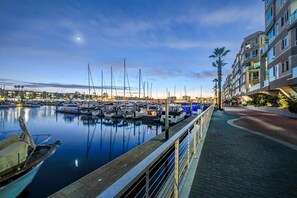A marina with boats docked, a waterfront promenade, and a modern building with balconies.