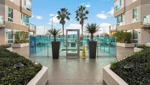 Een moderne hotelentree met een glazen deur, palmbomen en een heldere lucht.