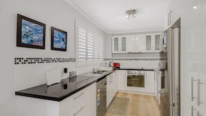 Una cocina moderna con armarios blancos, encimera negra, refrigerador de acero inoxidable y hervidor rojo.