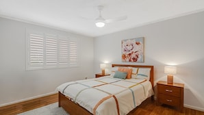 Un dormitorio con cama, mesitas de noche, ventilador de techo y ventana con persianas.