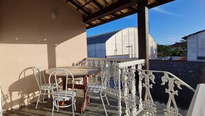 An outdoor patio with a round table and metal chairs, a decorative metal railing, and a view of a building in the background. - Holiday home accommodation for up to 12 people (Cabo Frio)