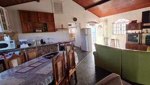 A spacious kitchen with wooden cabinets, a dining table with chairs, and a green sofa. - Holiday home accommodation for up to 12 people (Cabo Frio)