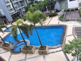 Zona de piscina en la azotea con palmeras, piscina y un edificio al fondo.