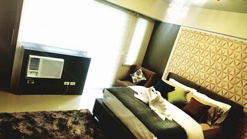 A hotel room with a bed, a wall-mounted air conditioner, and a window with blinds.