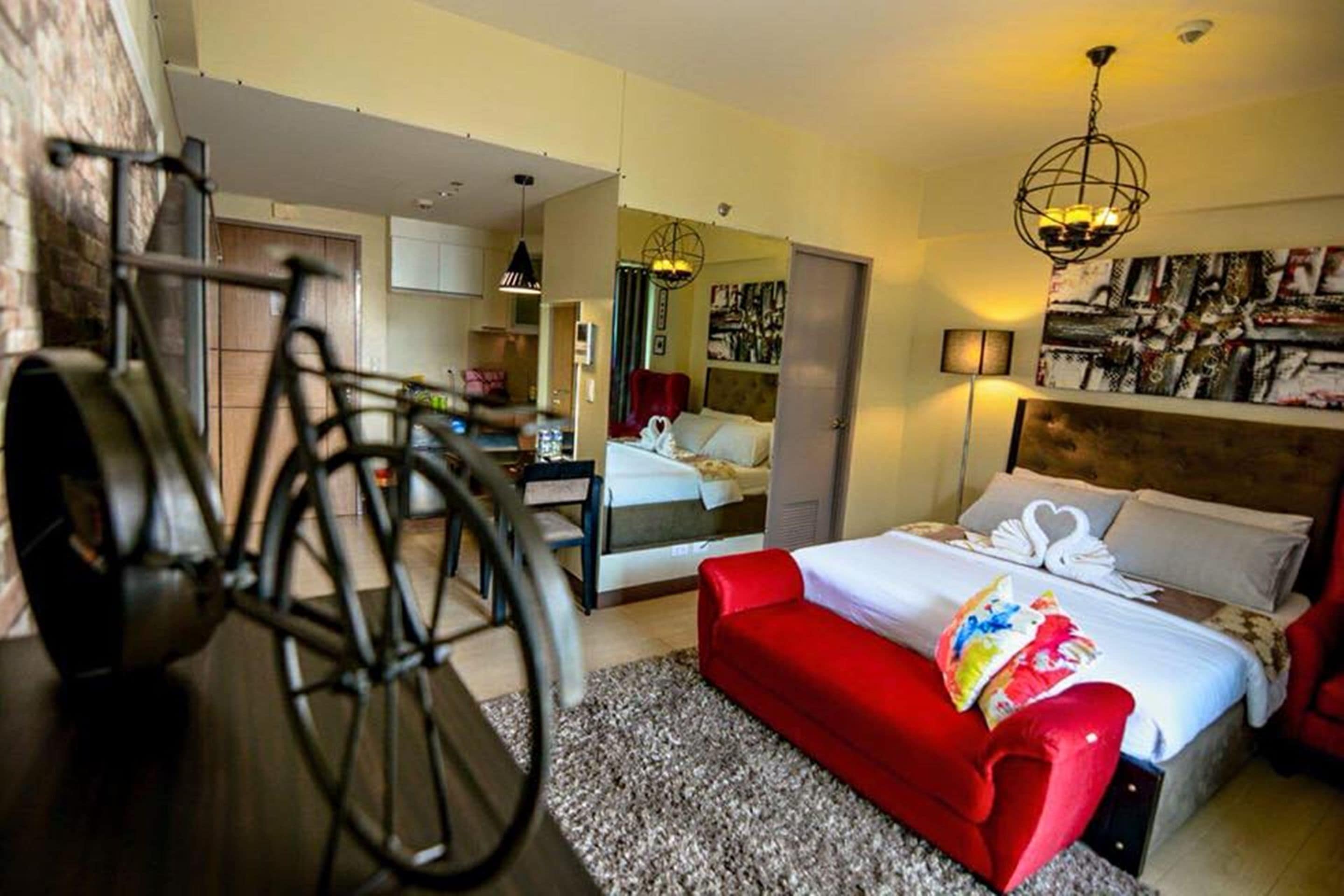 Une chambre d’hôtel avec un lit, un canapé rouge, un vélo et un miroir.
