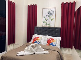 A hotel room with a bed, red curtains, a framed floral artwork, and a swan towel arrangement.