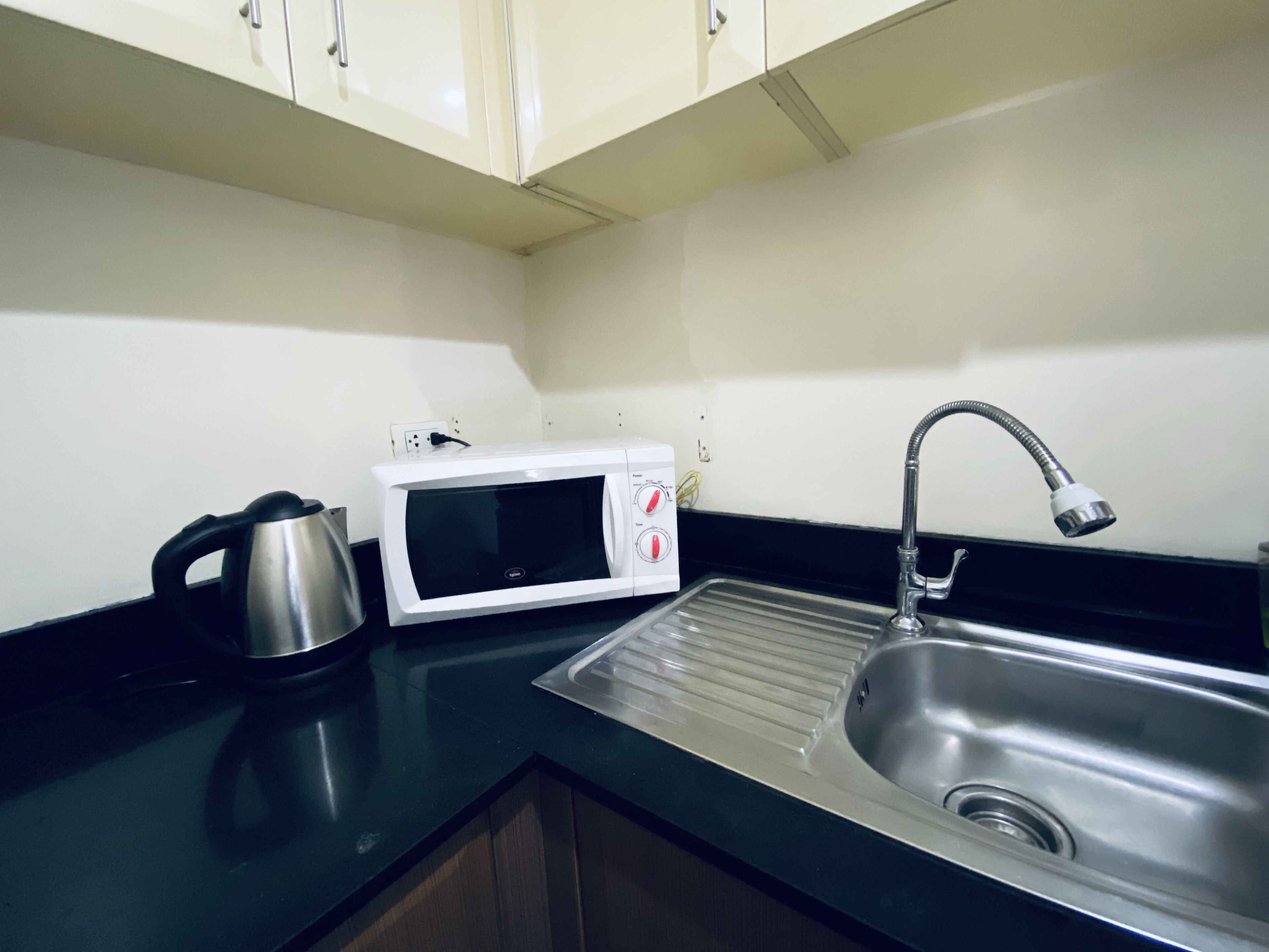 A kitchen with a stainless steel sink, a white microwave, and a kettle.