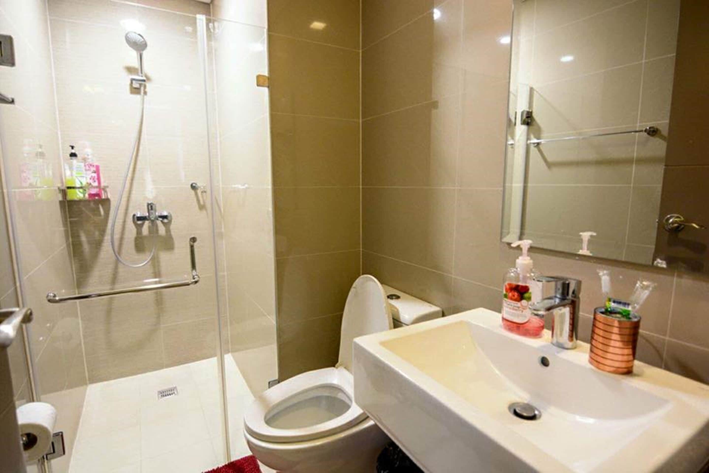 Un baño con cabina de ducha de vidrio, inodoro, lavamanos con artículos de aseo y espejo.