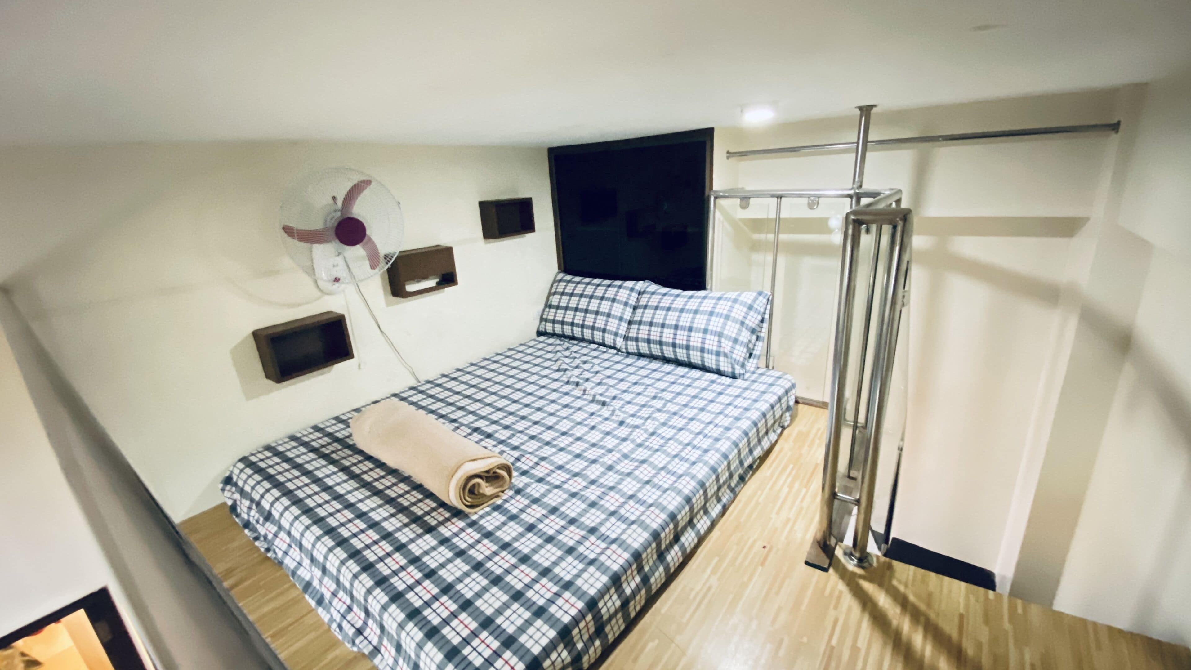 Un dormitorio con cama, ventilador de pared, televisor y zona de ducha.