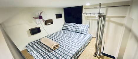 Un dormitorio con cama, ventilador de pared, televisor y zona de ducha.