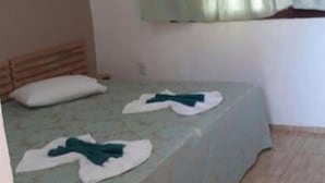 Una habitación pequeña y sencilla con una cama individual, un almohadón y una ventana con cortinas.