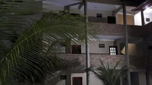 Un edificio de varios pisos con un patio, que incluye una palmera y una silla.