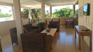 Un espacio al aire libre cubierto con mobiliario de mimbre, una mesa y un televisor montado en la pared.