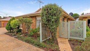 A residential house with a brick exterior, a driveway, and a garden with various plants and a fence. - Cosy Unit at 2-3 Wyndham in Cowes (Cowes)