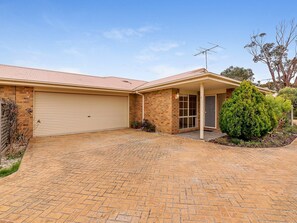 A two-story house with a garage, brick driveway, and a well-maintained lawn. - Cosy Unit at 2-3 Wyndham in Cowes (Cowes)