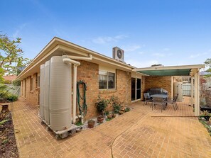 A residential backyard with a brick patio, a water tank, a barbecue area, and a covered seating space. - Cosy Unit at 2-3 Wyndham in Cowes (Cowes)