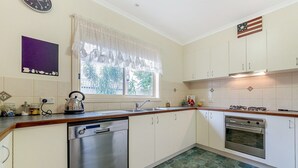 A kitchen with a dishwasher, stove, and window with lace curtains. - Cosy Unit at 2-3 Wyndham in Cowes (Cowes)