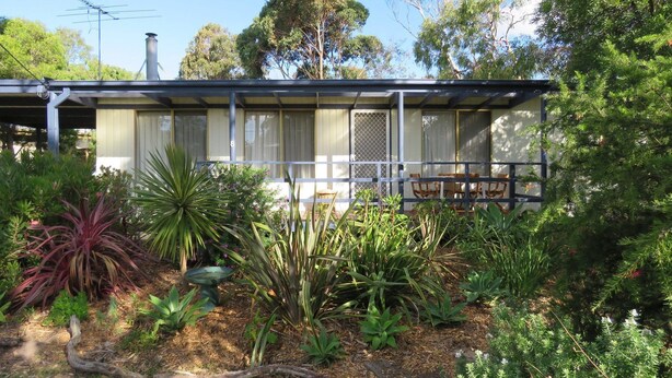 A single-story house with a covered porch, surrounded by various plants and trees. - 8 Ophir Cottage in Ventnor (Ventnor)