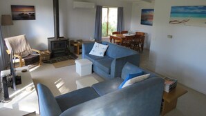 A living room with a sofa, a chair, a fireplace, a dining table with chairs, and paintings on the walls. - 8 Ophir Cottage in Ventnor (Ventnor)
