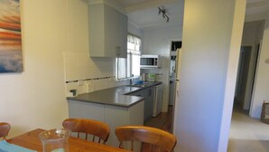 A compact kitchen with a central island, a dining table with chairs, and a view into the living area. - 8 Ophir Cottage in Ventnor (Ventnor)