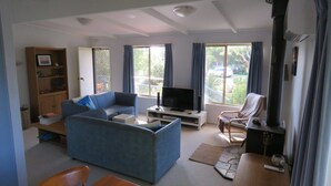 A living room with a blue sofa, a TV, a fireplace, and a dining area with a table and chairs. - 8 Ophir Cottage in Ventnor (Ventnor)
