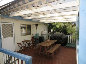 A covered patio with wooden furniture, a grill, and a window overlooking greenery.