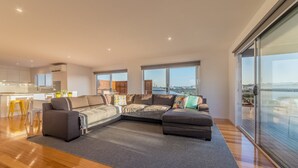 A modern living room with a sectional sofa, a dining area with yellow stools, and a large sliding glass door leading to a balcony with a view of a bridge and water. - 7 Boardwalk Lakeside in Cowes (Cowes)